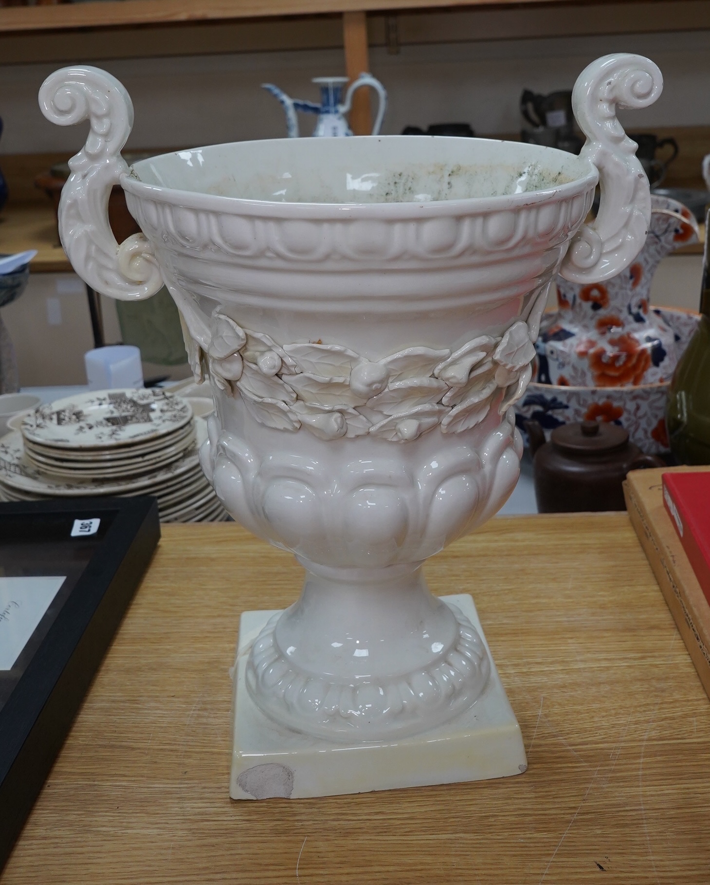 A large cream glazed pottery pedestal vase, with decorative swag of fruit and leaves, 43cm high. Condition - corner of square base broken, glazing chipped on top rim and fruit and leaf decoration broken